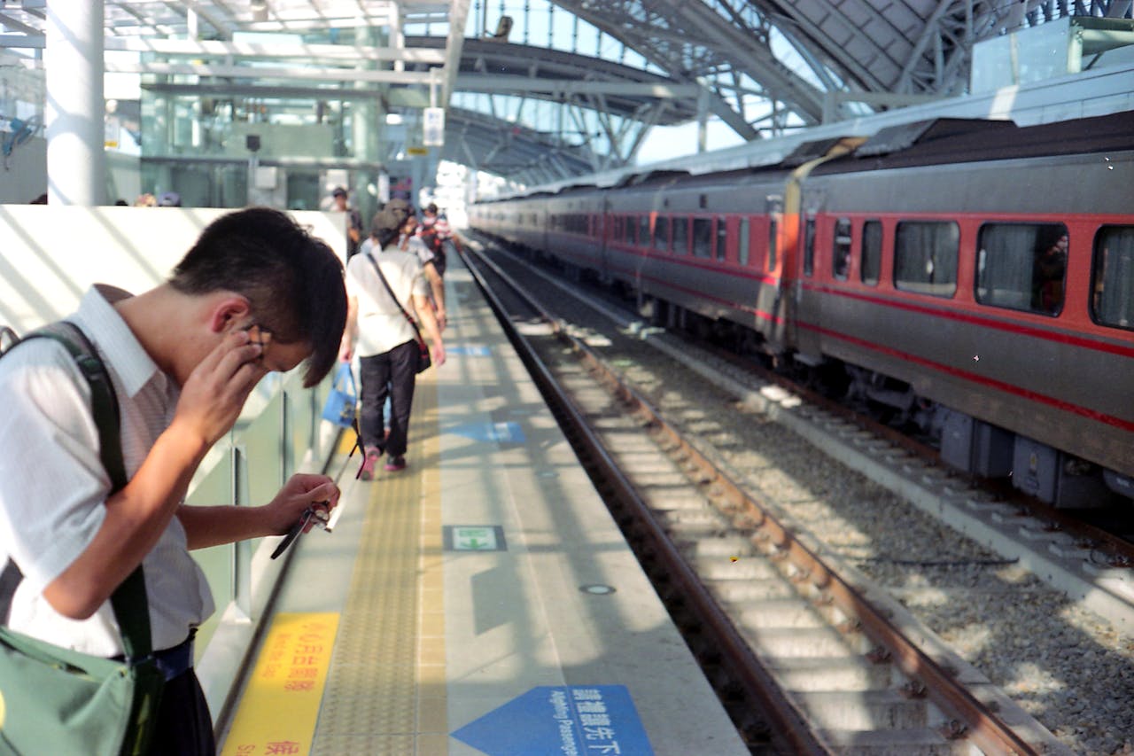 why-choose-us Commuters on a railway platform in Taichung, Taiwan, near a red and black train.